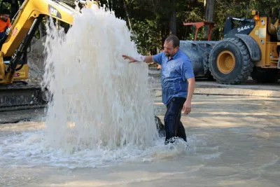 File photo of Jason Kytle working water line break in the road with large geyser of water.